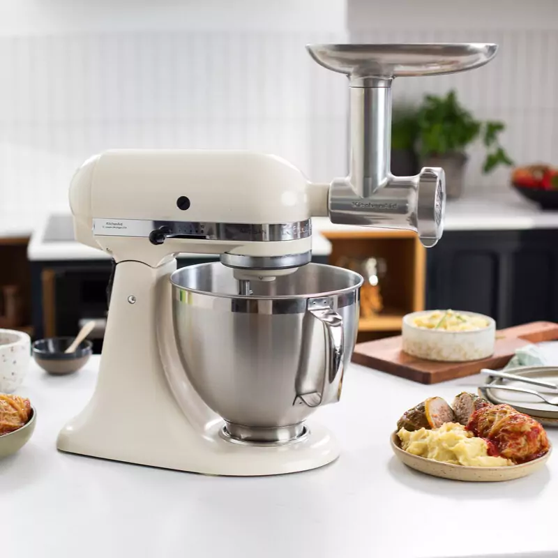 HR: KitchenAid samostojeći mikser u boji Almond cream s nastavkom za mljevenje hrane u kuhinjskom okruženju.